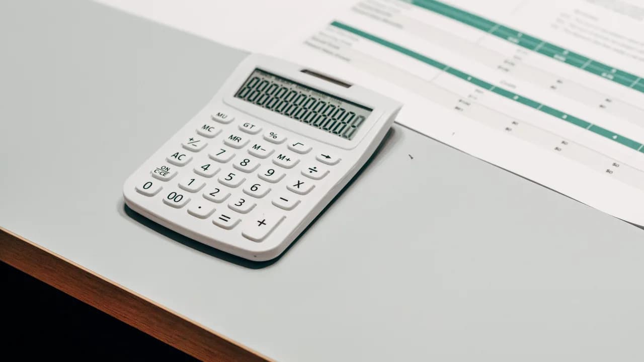 Een rekenmachine, een pen en uitgeprinte werkbladen op een bureau
