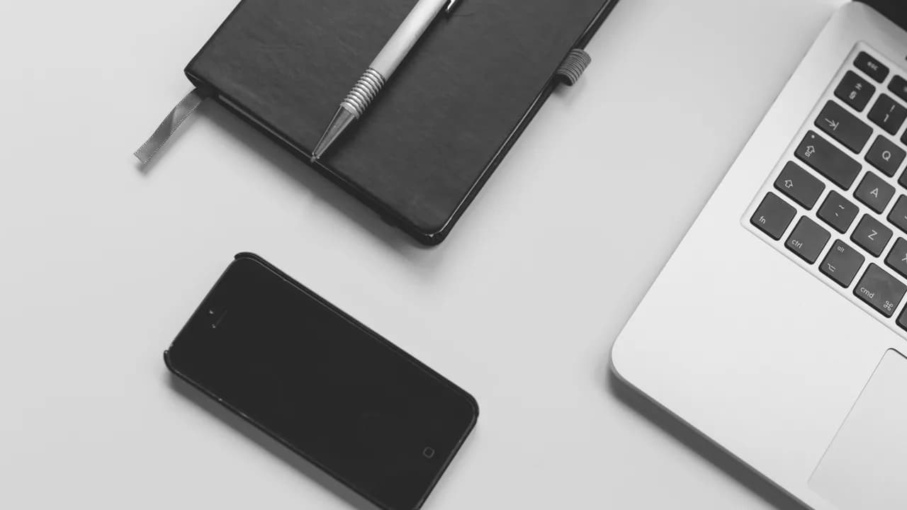 Ein Notizbuch, ein Stift, ein Handy und ein Laptop auf einem Tisch